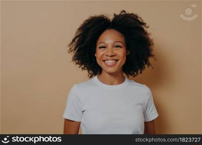 Beautiful young african female smiling cheerfully at camera and demonstrating happiness, standing against color wall in studio,dark skinned woman in casual outfit with curly hair showing white teeth. Beautiful young african female smiling cheerfully at camera and demonstrating happiness