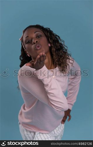 Beautiful young african woman sending air kiss on blue background