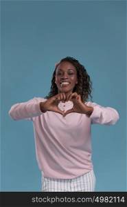 Beautiful young african woman showing heart symbol with fingers on blue background