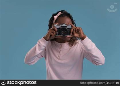 Beautiful young african woman using camera and photographing on blue background