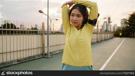 Beautiful young Asia athlete lady exercises using smartphone for listen to music while running in urban environment. Korean teen girl wearing sports clothes on walkway bridge in early morning.