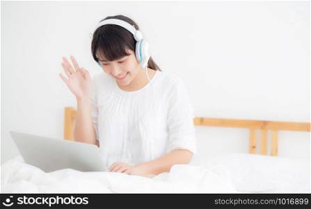 Beautiful young asia woman lying in bedroom using laptop computer showing video call chat at home, girl greet and listen and talking messenger, communication and lifestyle concept.