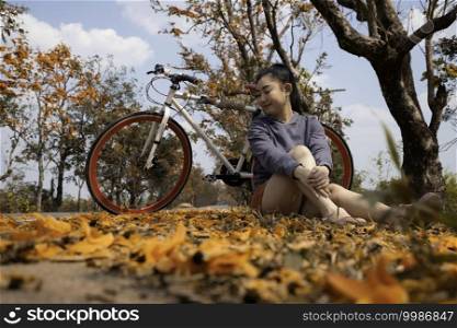 Beautiful young asia woman sitting next to her bike outdoors at palash tree with full of beautiful orange flower background, Butea Monosperma or Butea frondosa of southeast asia from nature 