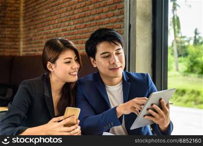 beautiful young asian businesswoman hold mobile phone and businessman look at tablet for business project