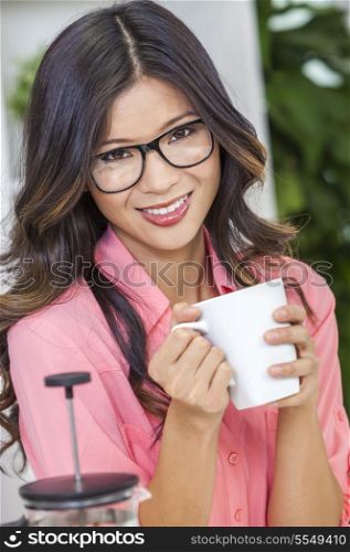Beautiful young Asian Chinese woman or girl in geek glasses at home in her kitchen smiling and drinking a cup or mug of coffee