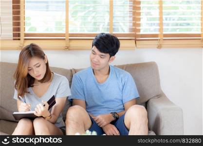 Beautiful young asian couple planning and writing on notepad or diary, family list purchase, man and woman cheerful studying and read for education, family relax, lifestyle and wellbeing concept.