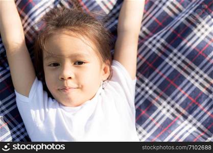 Beautiful young asian girl lying down and smiling on mat in the park, asia child portrait relax and leisure in vacation, kid laugh fun and happy in spring and summer, lifestyle childhood concept.