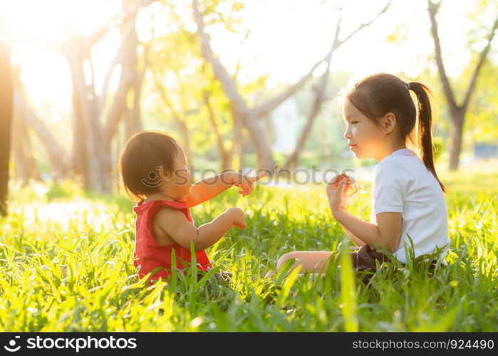 Beautiful young asian kid sitting playing in summer in the park with enjoy and cheerful on green grass, children activity with relax and happiness together on meadow, family and holiday concept.