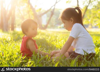 Beautiful young asian kid sitting playing in summer in the park with enjoy and cheerful on green grass, children activity with relax and happiness together on meadow, family and holiday concept.