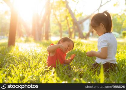Beautiful young asian kid sitting playing in summer in the park with enjoy and cheerful on green grass, children activity with relax and happiness together on meadow, family and holiday concept.