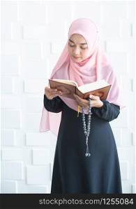 Beautiful young asian muslim woman dress hijab standing and reading quran holding beads