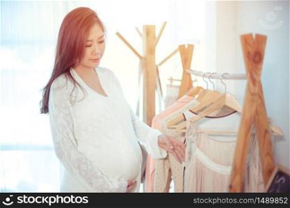 Beautiful young asian pregnant woman choosing what to wear