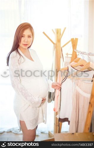 Beautiful young asian pregnant woman choosing what to wear