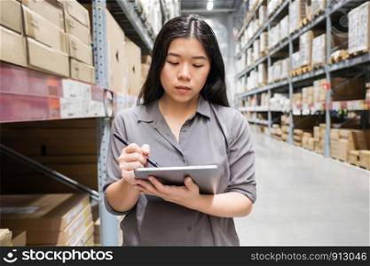 Beautiful young Asian woman auditor or trainee staff work stocktaking with computer tablet at warehouse store, Asian working business woman concept