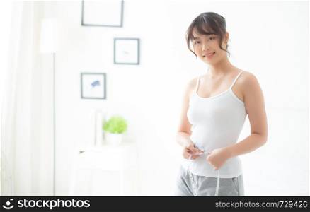 Beautiful young asian woman body diet and slim with measuring waist for weight in the bedroom, girl have cellulite and calories loss with tape measure, health and wellness concept.