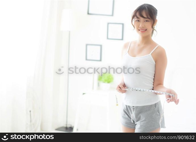 Beautiful young asian woman body diet and slim with measuring waist for weight in the bedroom, girl have cellulite and calories loss with tape measure, health and wellness concept.