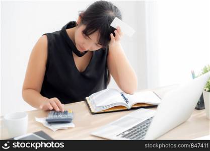 Beautiful young asian woman calculating expenses household and writing notebook on desk, girl checking bill and stress and note, female worry debt and tax, finance and business concept.