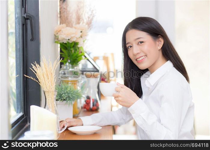 Beautiful young asian woman drinking coffee and smile in the morning at cafe, girl sitting in coffee shop for breakfast and leisure during free time.
