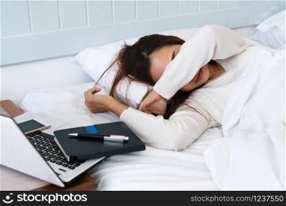 Beautiful young asian woman feel tired and lie down on bed with her pending work aside, working on bed , work at home, busy lifestyle concept.