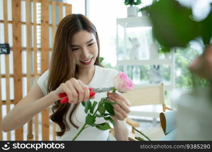 Beautiful young asian woman florist cutting rose flower in flower shop