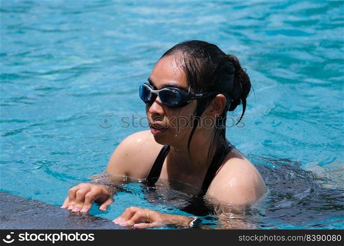 Beautiful young asian woman happy and smile in swimming pool. Asian woman in swimsuit is swimming in the blue clean water of the swimming pool for exercise. Travel and summer vacation concept.