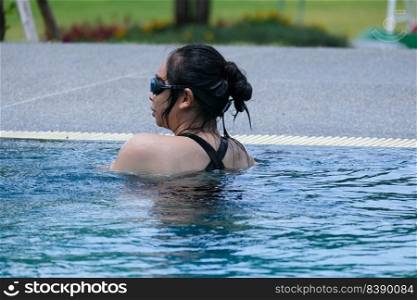 Beautiful young asian woman happy and smile in swimming pool. Asian woman in swimsuit is swimming in the blue clean water of the swimming pool for exercise. Travel and summer vacation concept.