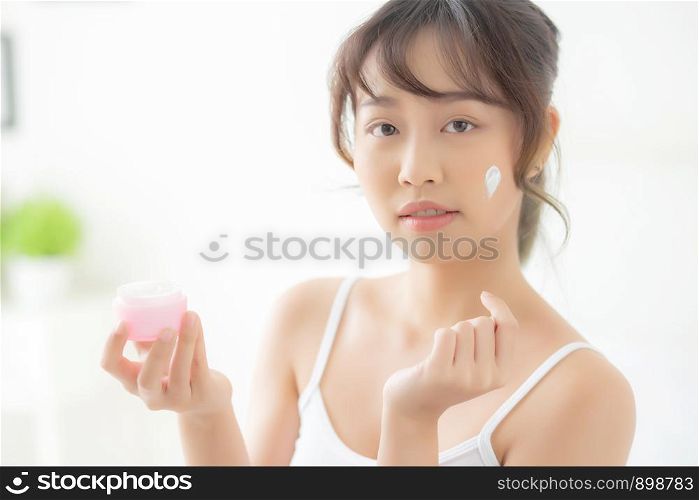 beautiful young asian woman happy applying cream or lotion with moisturizer to skin face, beauty asia girl applying skincare touch facial with cosmetic makeup, healthy and wellness concept.