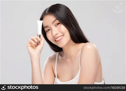 Beautiful Young Asian Woman Holding luxury white clean tube smile feeling so happy and cheerful with healthy Clean and Fresh skin,isolated on gray background,Beauty Cosmetics Concept