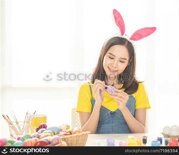 Beautiful young asian woman painting easter eggs on table with decorated eggs for celebrate April Easter day with copy space.