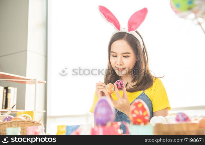 Beautiful young asian woman painting easter eggs on table with decorated eggs for celebrate April Easter day with copy space.