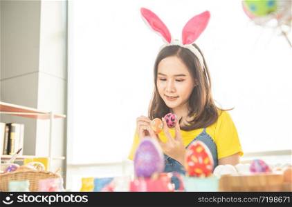 Beautiful young asian woman painting easter eggs on table with decorated eggs for celebrate April Easter day with copy space.
