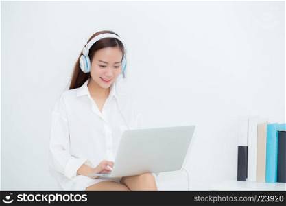 Beautiful young asian woman relax with wear headphone enjoy listening music using laptop computer, girl working laptop on chair in the living room, communication and lifestyle concept.