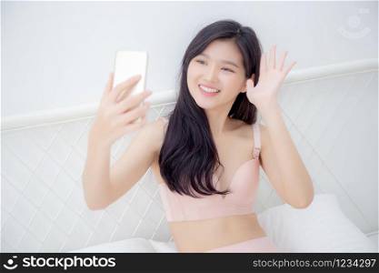 Beautiful young asian woman sexy in underwear talking a selfie on smartphone for social network in the bedroom, girl in lingerie relax with taking a picture on mobile phone on bed in the bedchamber.