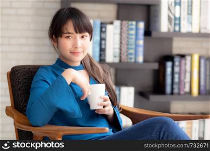 Beautiful young asian woman sitting on chair with comfort and relaxing in living room at home drinking a cup of coffee or tea or beverage, lifestyle asia girl leisure healthy and wellness for satisfied.