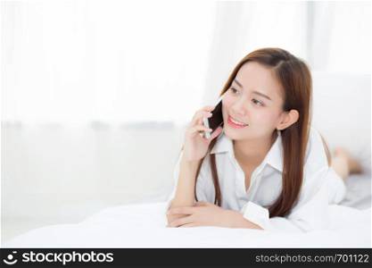Beautiful young asian woman smiling lying and relax on the bed in the morning, girl using mobile smart phone talking enjoy, communication concept.