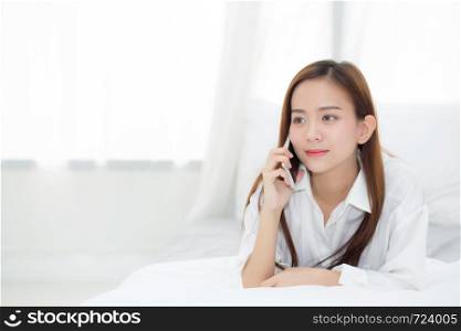Beautiful young asian woman smiling lying and relax on the bed in the morning, girl using mobile smart phone talking enjoy, communication concept.