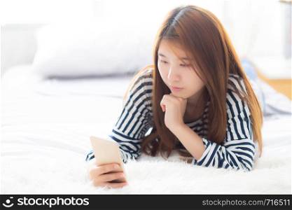 Beautiful young asian woman smiling lying relax on the bed in the morning, girl using mobile smart phone talking enjoy, communication and social network concept.