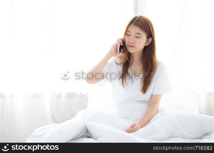 Beautiful young asian woman smiling sitting and relax on the bed in the morning, girl using mobile smart phone talking enjoy at bedroom, communication concept.