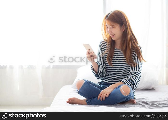 Beautiful young asian woman smiling sitting relax on the bed in the morning, girl using mobile smart phone talking enjoy, communication and social network concept.