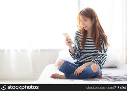 Beautiful young asian woman smiling sitting relax on the bed in the morning, girl using mobile smart phone talking enjoy, communication and social network concept.