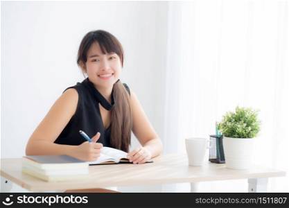 Beautiful young asian woman smiling sitting study and learning writing notebook and diary in the living room at home, girl homework, business woman working on table, education concept.
