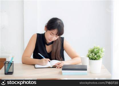 Beautiful young asian woman smiling sitting study and learning writing notebook and diary in the living room at home, girl homework, business woman working on table, education concept.