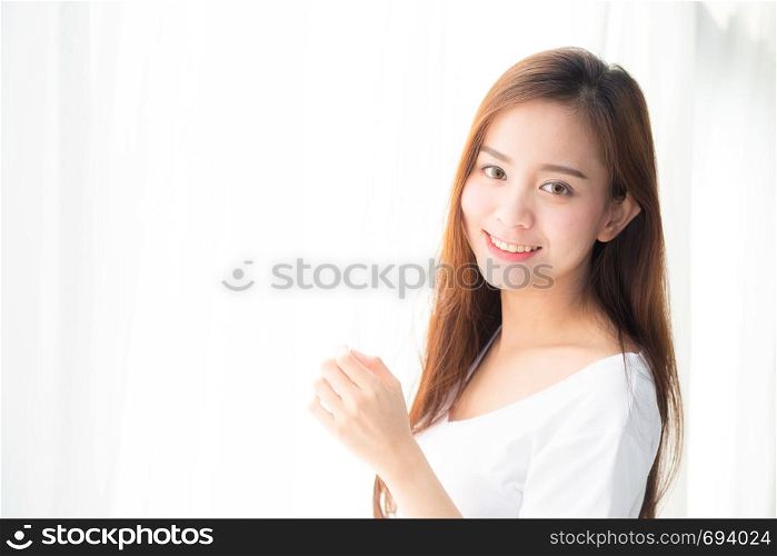 Beautiful young asian woman standing the window and smile while wake up with sunrise at morning, lifestyle and relax concept.