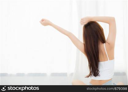 Beautiful young asian woman stretch and relax in bed after wake up morning at bedroom, back view, new day and resting for wellness, lifestyle concept.
