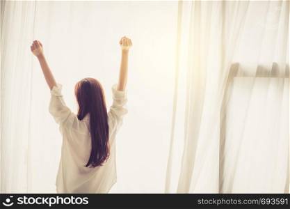 Beautiful young asian woman stretch and relax in bed after wake up morning at bedroom, back view, new day and resting for wellness, lifestyle concept.