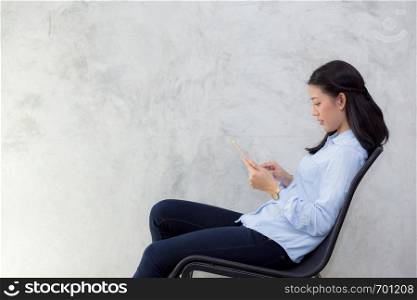 Beautiful young asian woman touching tablet computer and smile sitting on cement background, freelancer female calling telephone, communication concept.