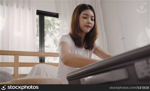 Beautiful young Asian woman traveler packing stuff in suitcase prepare for holiday vacation while lying on the bed when relax in her bedroom at home. Lifestyle women backpacker travel concept.