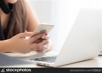 Beautiful young asian woman working laptop computer online to internet and texting message on smart mobile phone, freelance using notebook, business and communication concept.