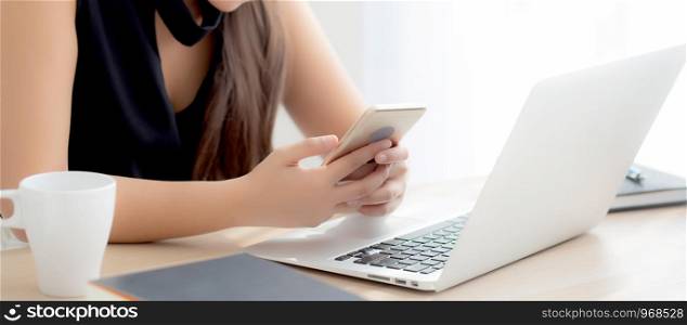 Beautiful young asian woman working laptop computer online to internet and texting message on smart mobile phone, freelance using notebook, business and communication concept.