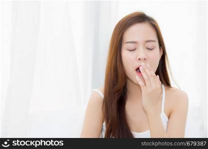 Beautiful young asian woman yawn sitting with sleep on bed at bedroom, girl wake up after resting and leisure with wellness, lifestyle concept.